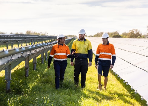 Three men high vis walking along a grass path through a solar panel farm