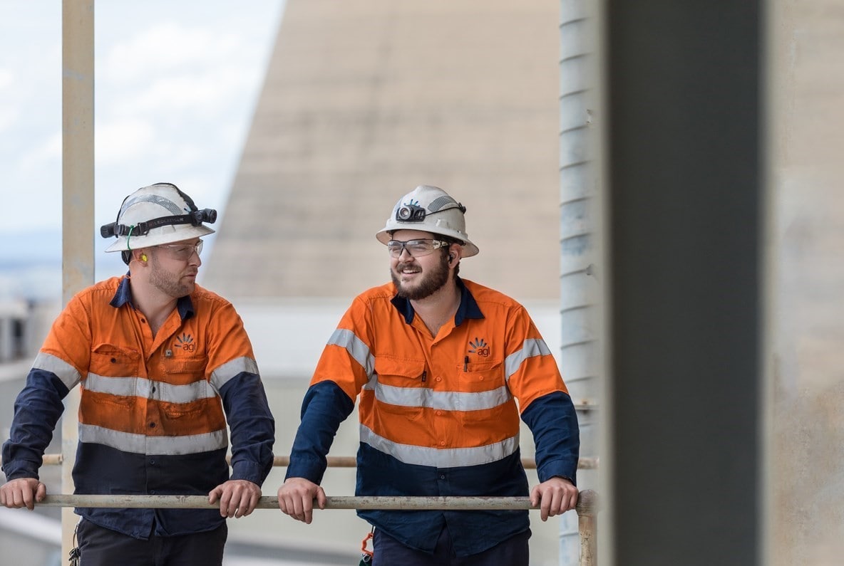 Two men in hi-vis hardhats talking in an industrial setting.