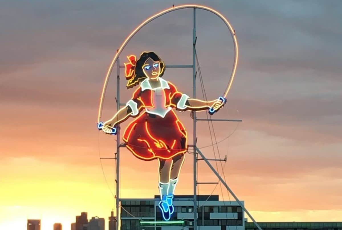 Iconic 'Skipping Girl' neon sign illuminated at twilight.