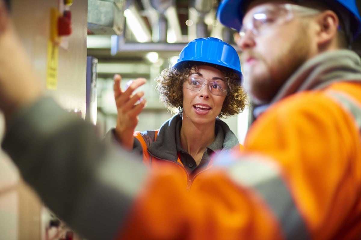 Male and female co-workers in orange high viz, safety goggles and blue hard hats