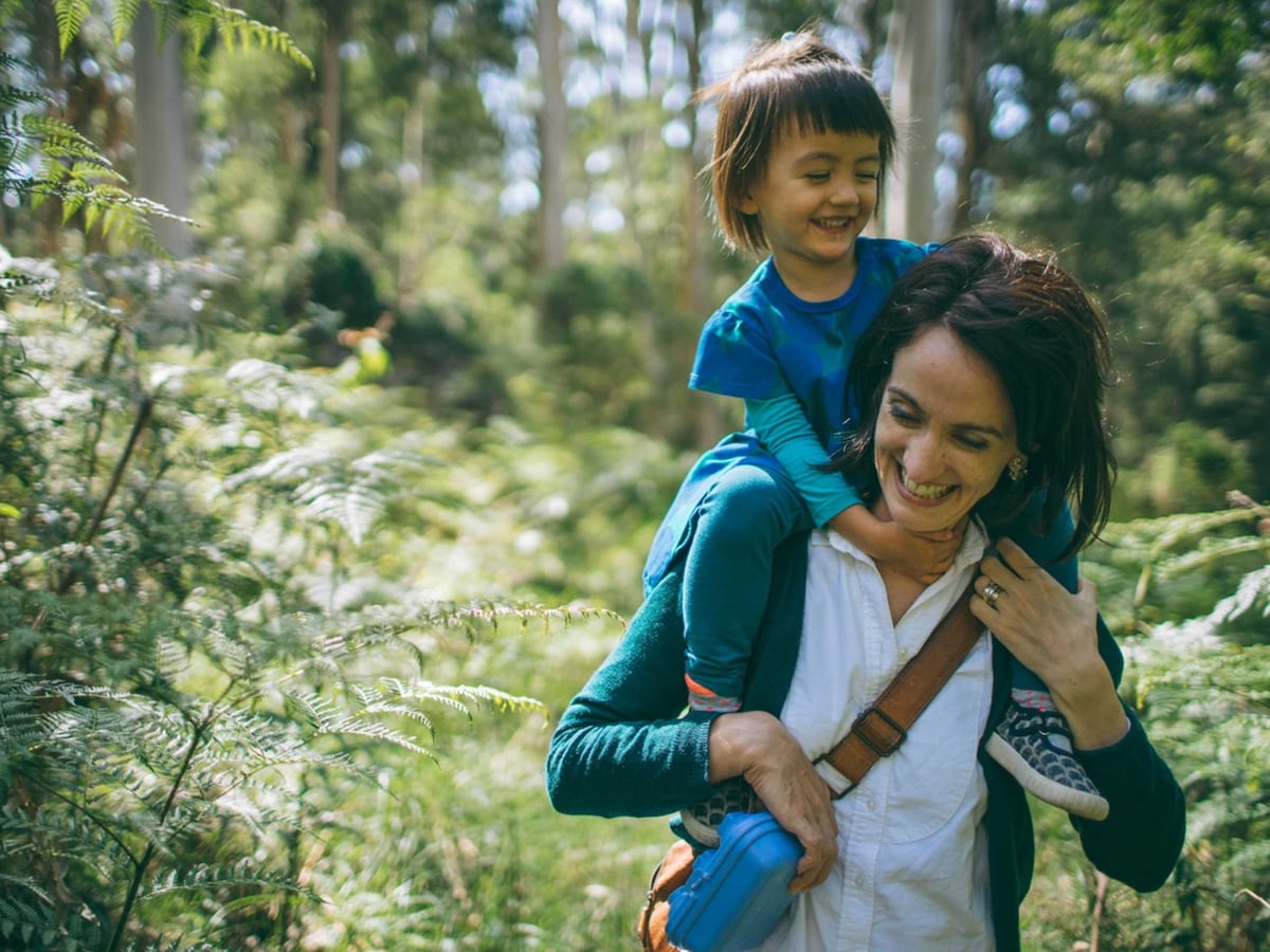 A woman with her child on her shoulders bushwalking