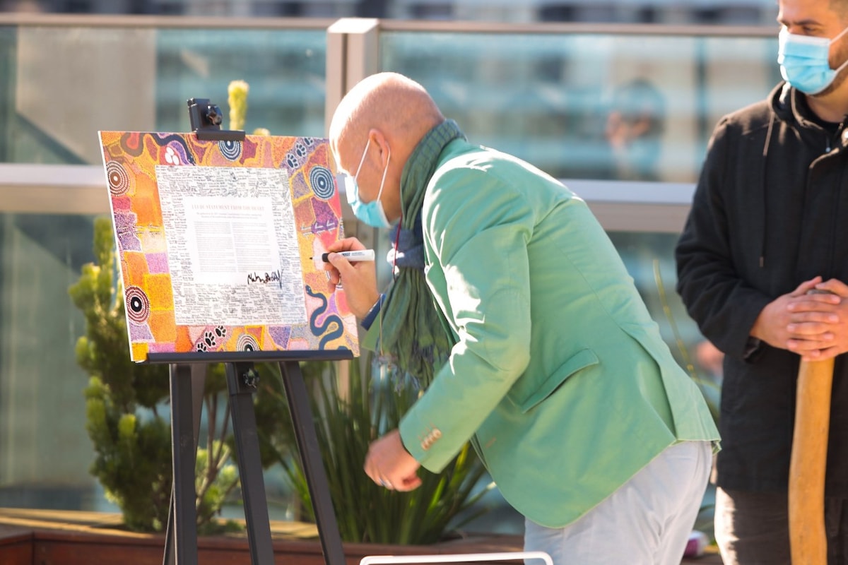 Signing the Uluru Statement from the Heart, surrounded by indigenous artwork.