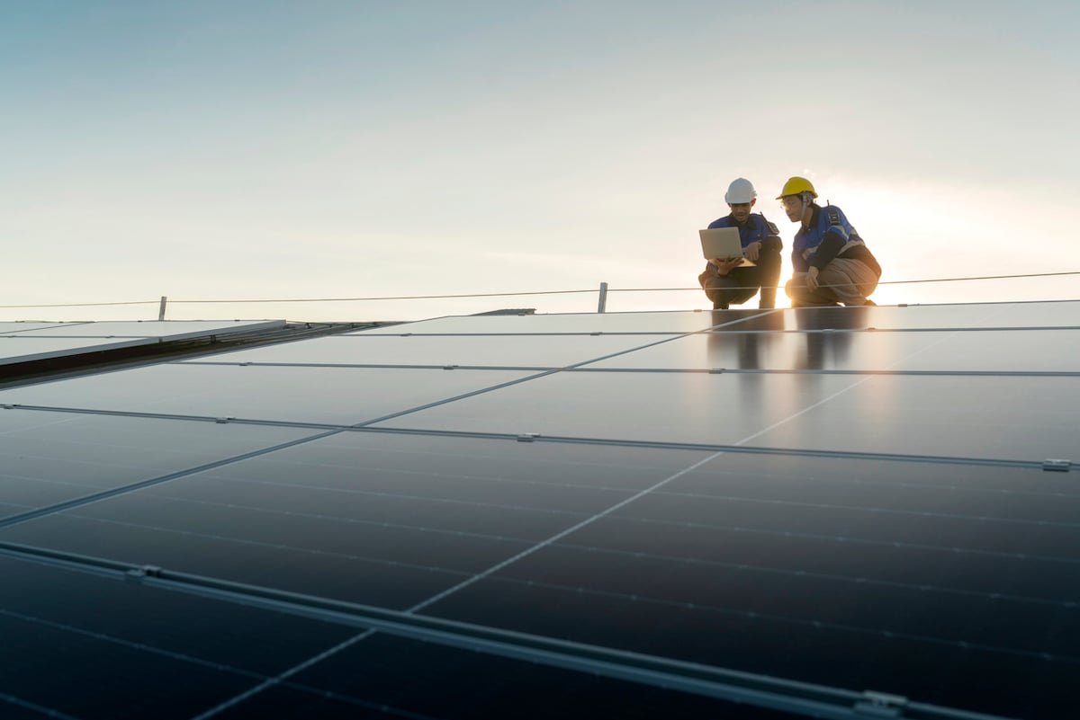 Two tradies crouching over solar panels in a solar farm at sunrise