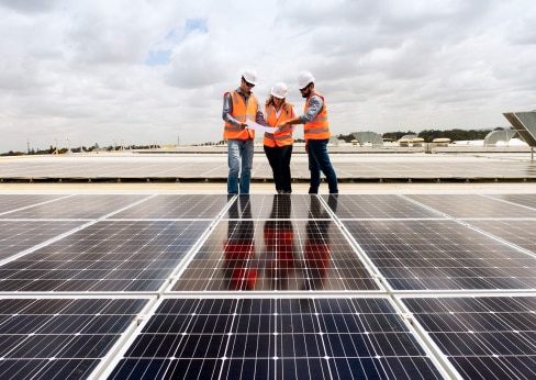 Three workers in high vis inspecting solar panels