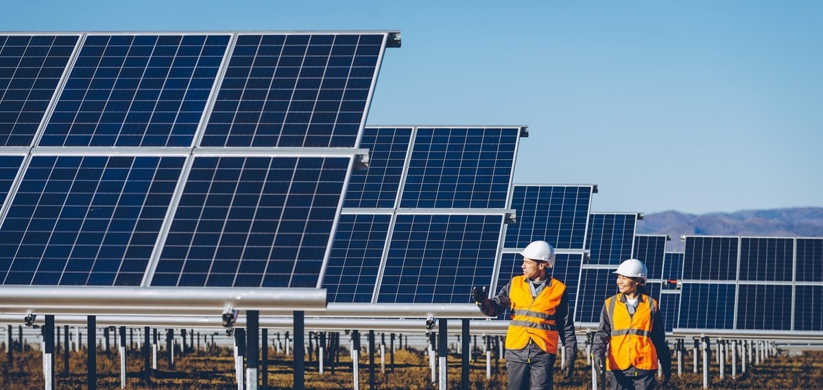 Two people in high vis vests and hardhats walking amongst large solar panel arrays on a solar farm