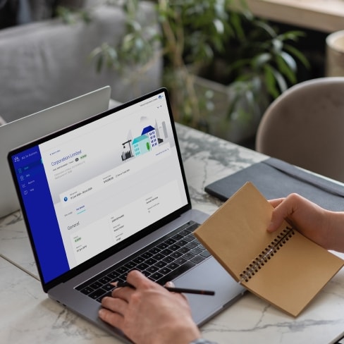 Person working from a laptop dashboard while holding a pen and notebook