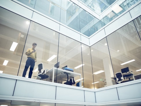 Man standing looking down through a glass office wall