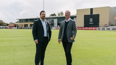 Two men dressed in suits standing on a sports field posing for a photo