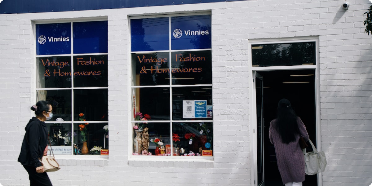 Front of charity shop with person walking past window wearing a mask