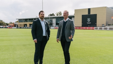 Two men dressed in suits standing on a sports field posing for a photo