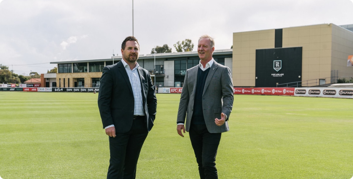 Two men dressed in suits standing on a sports field posing for a photo