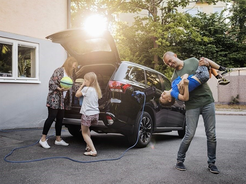Mother and father and two kids having fun next to a plugged in electric vehicle.