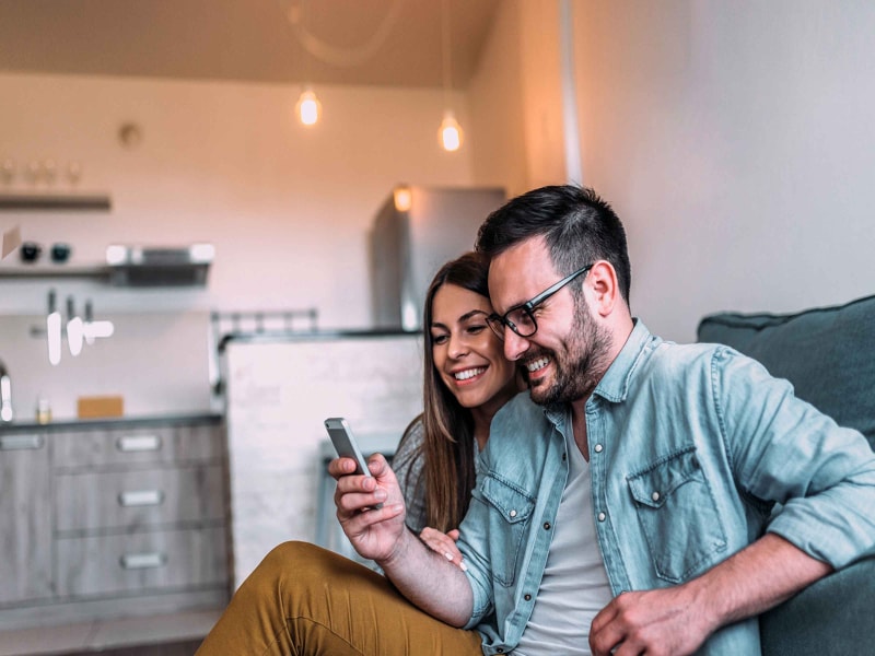 Man and woman scrolling through phone while sitting on couch