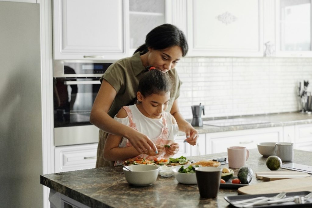 Child stiring food on stove with parent watching