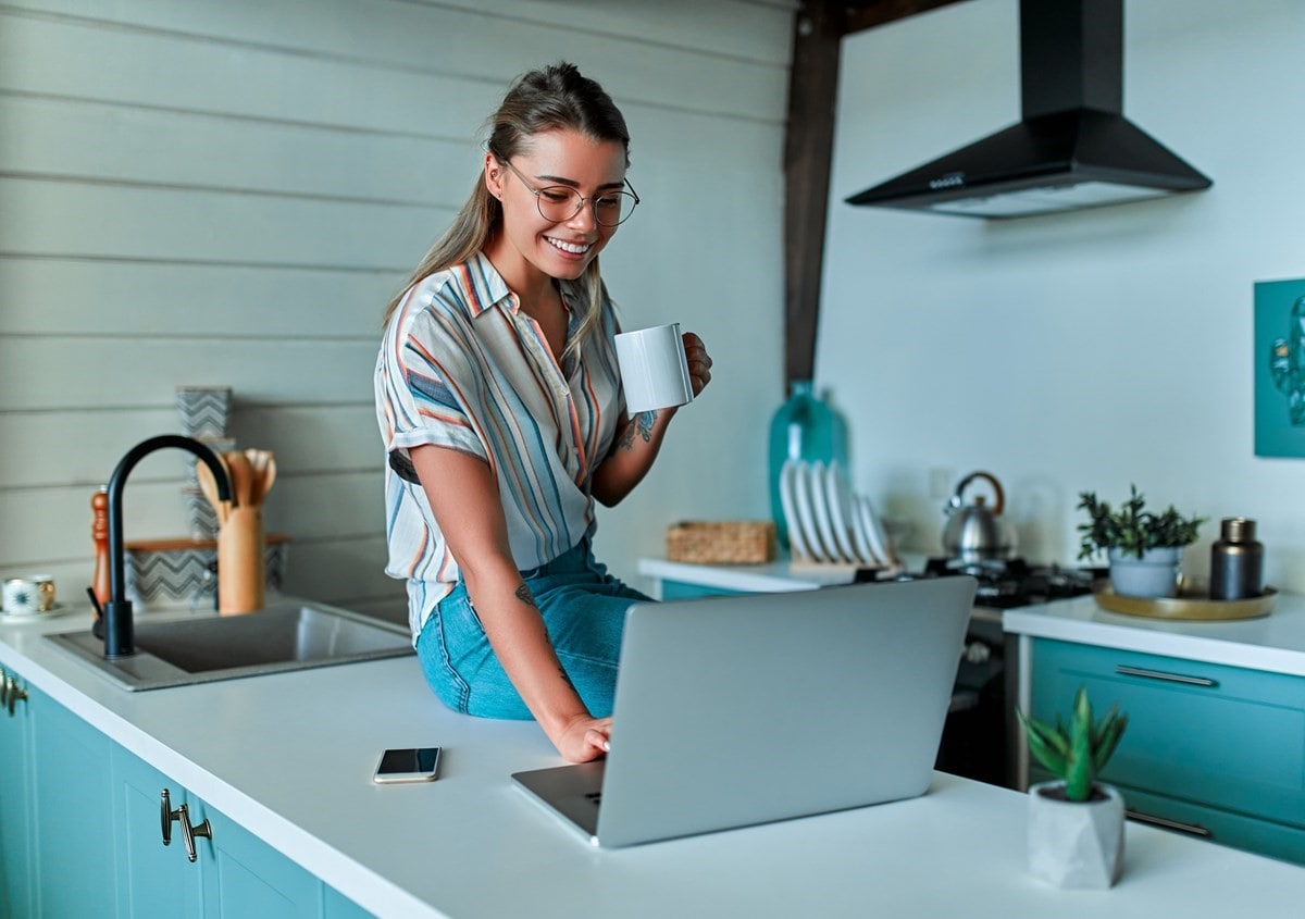 A woman sitting on her kitchen bench looking at her laptop
