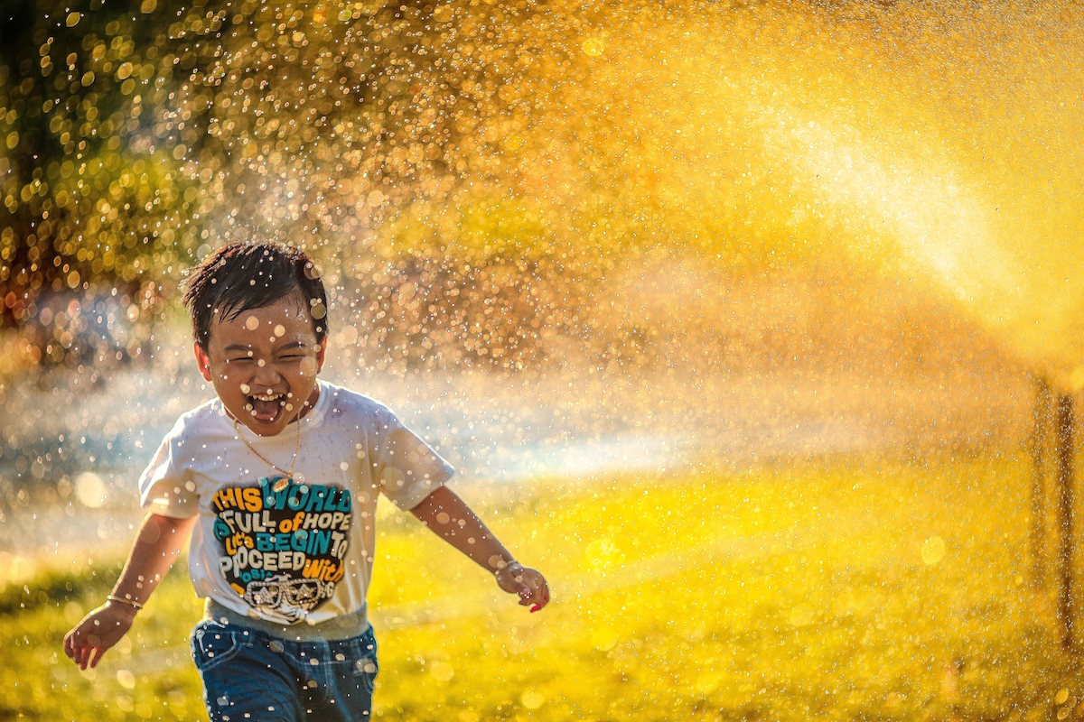 Young boy running through garden sprinkler at sunset