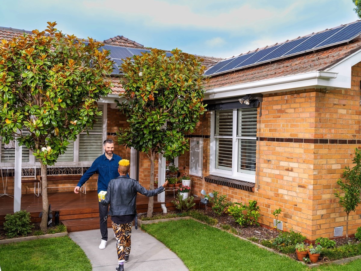 Friends greeting each other outside brick home with solar panels