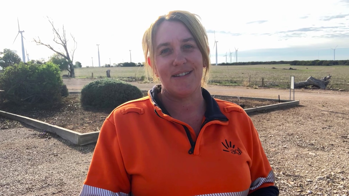 Photo of Chloe smilling in high vis jumper with wind farm in the background. 