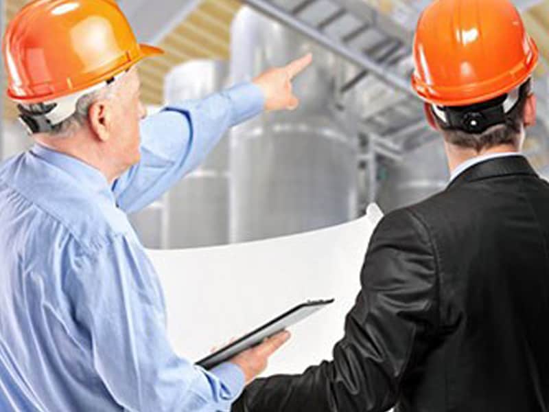 Image of two men in hard hats, surveying a work site. 