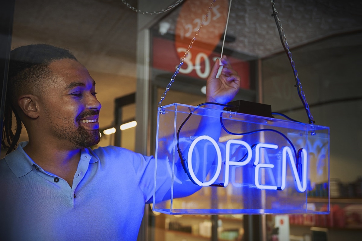 Man standing behind an 'open' sign in a business