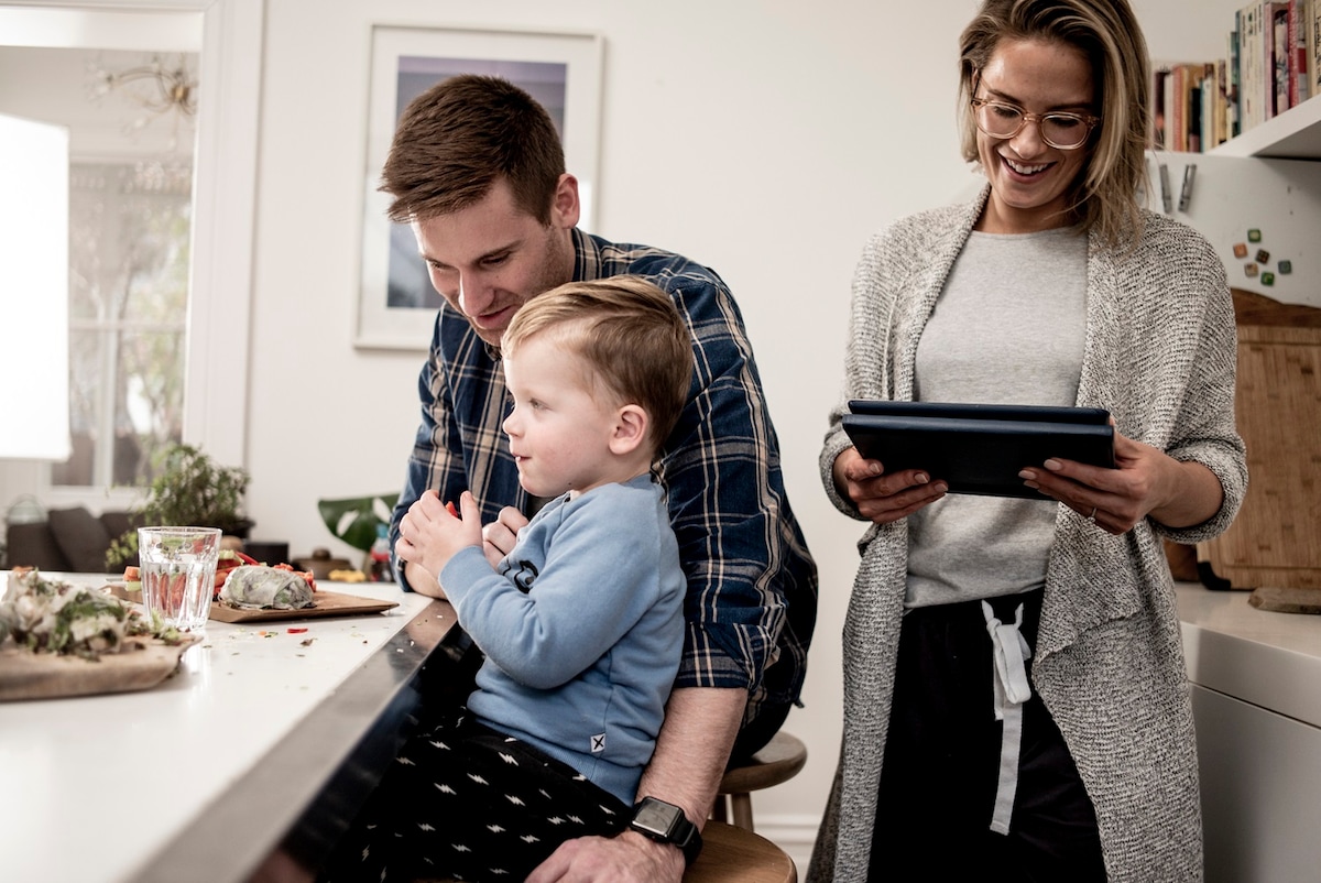 A man, woman and child in the kitchen eating snacks and chatting