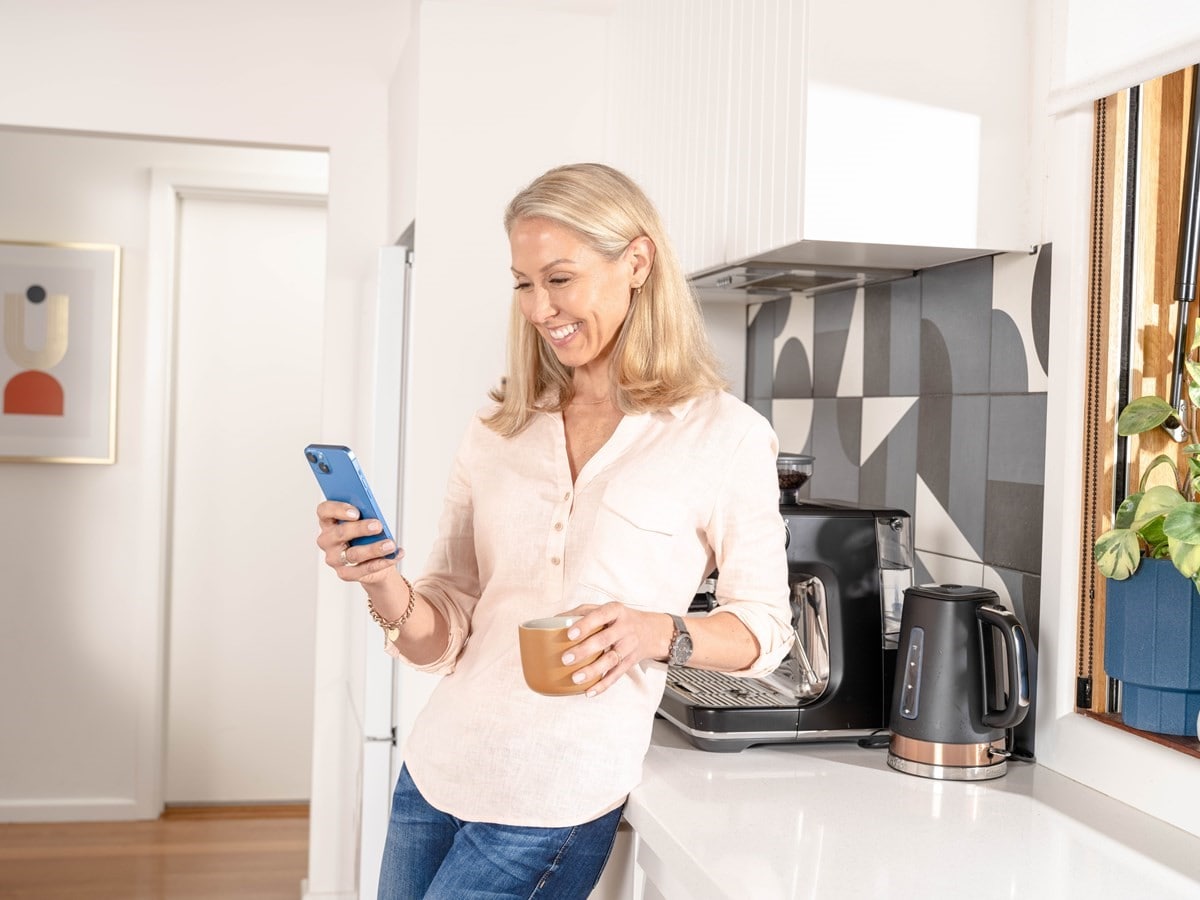 Photo of a woman chatting with the AGL Virtal assistant on her phone with a cup of coffee