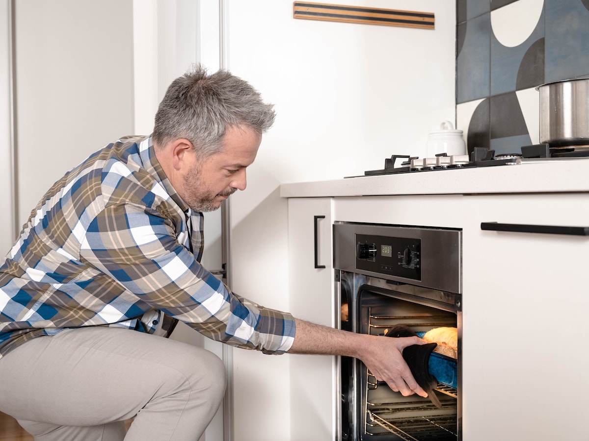 A man taking a baked dish out of the oven in a kitchen
