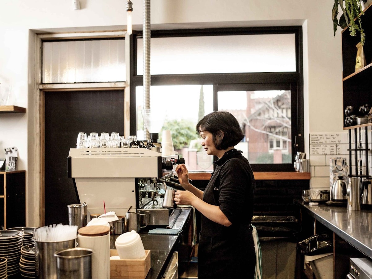 A female barista standing behind a coffee machine making a cup of coffee