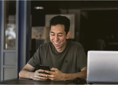 Man smiling at his phone in a dimly lit room 