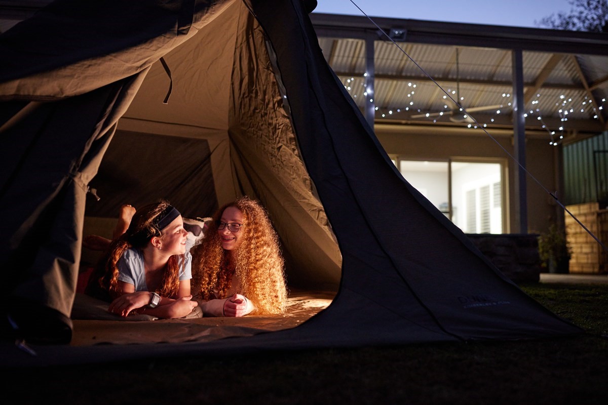 Two kids camping in a tent in their backyard