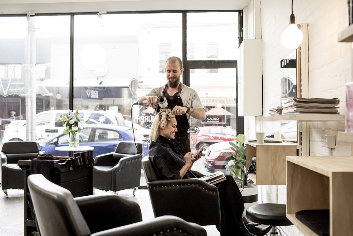 Woman at hairdresser, male hairdresser blow drying her hair