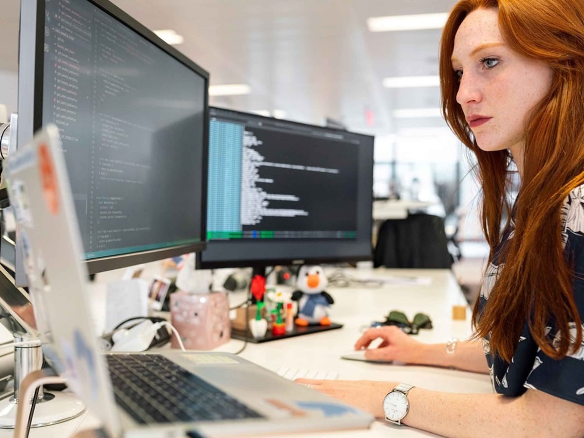 Woman at desk with laptop and two computer screens in front of her