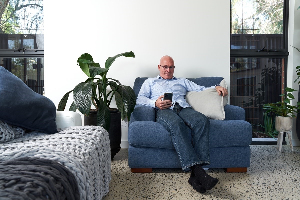 Darren, VPP customer, sitting on armchair with mobile in living room