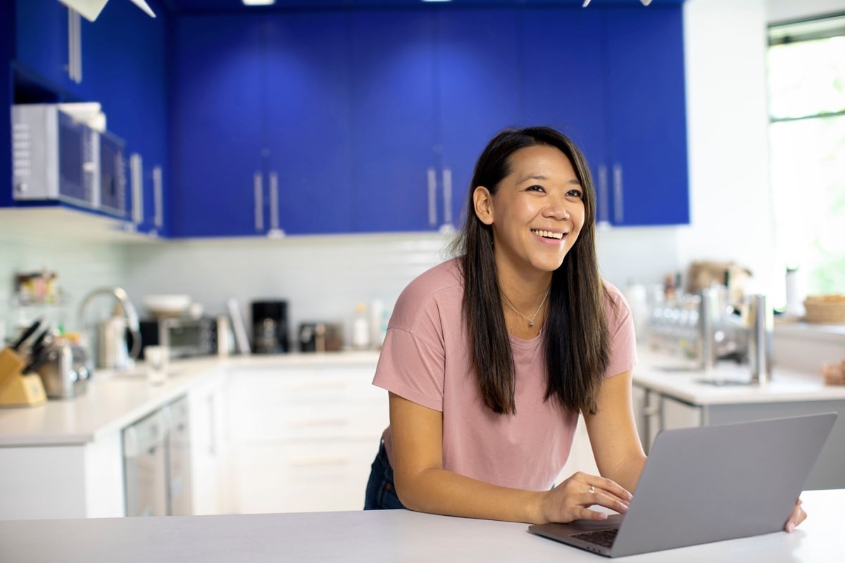 Woman smiling using her laptop in kitchen