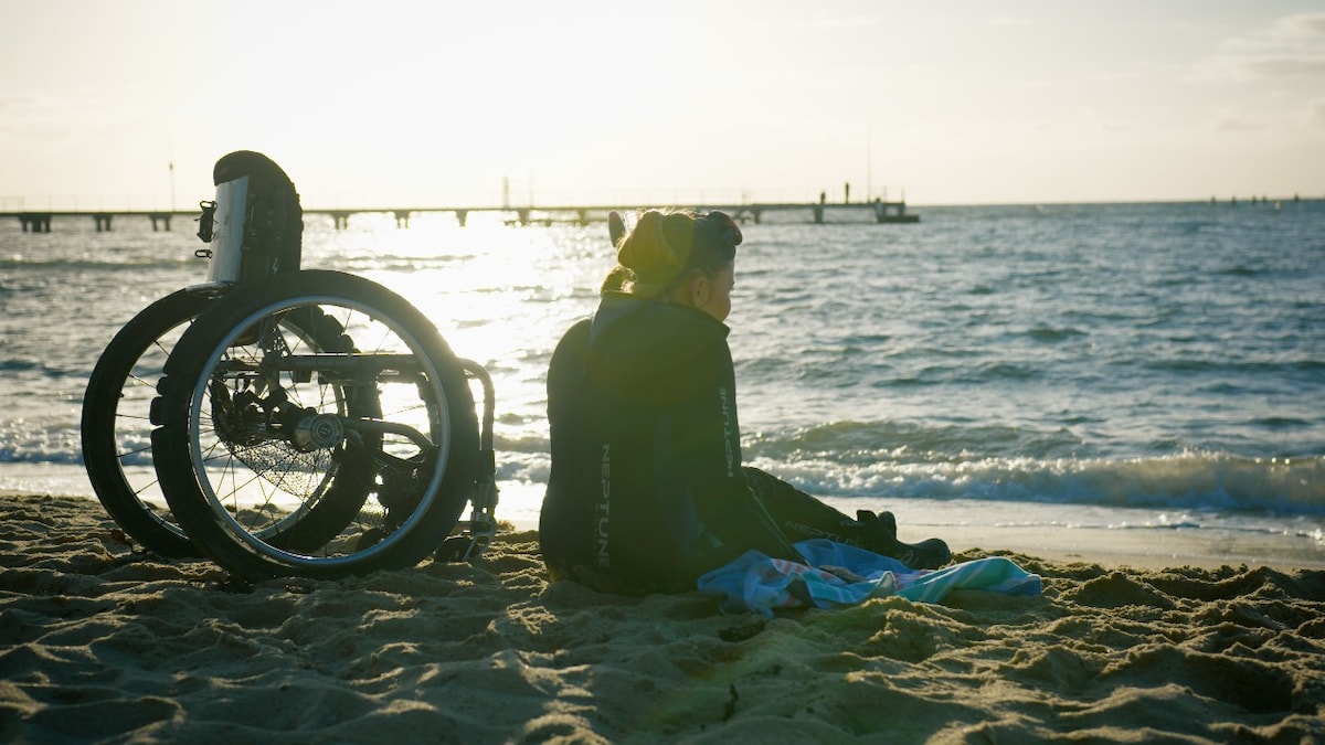 Wheelchair user sitting on the sand at sunset