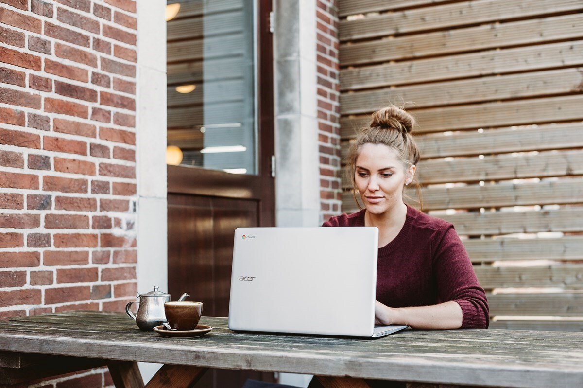 A woman typing on her laptop on an outside wooden caf table