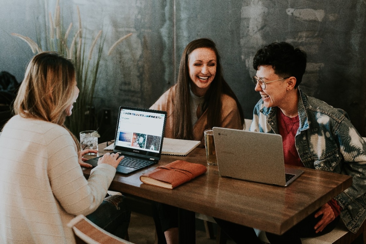 Young women at cafe laughing while using their laptops
