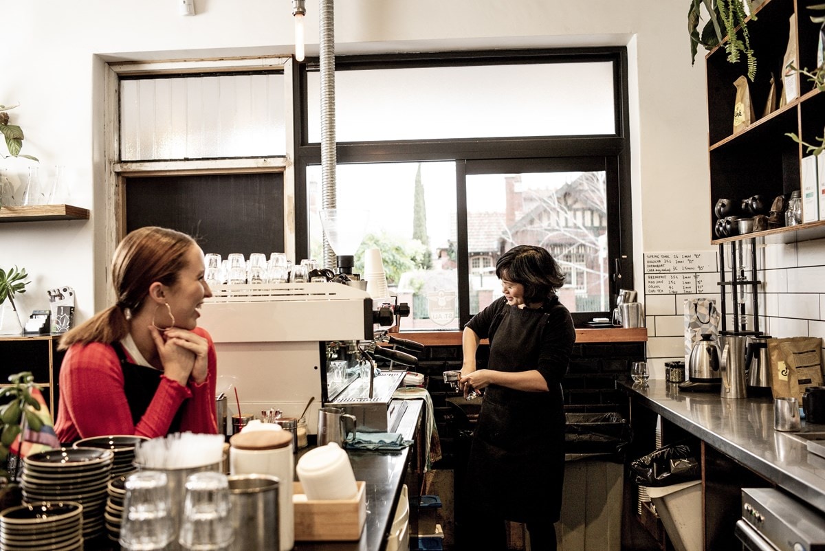 Two women working in a cafe serving coffee