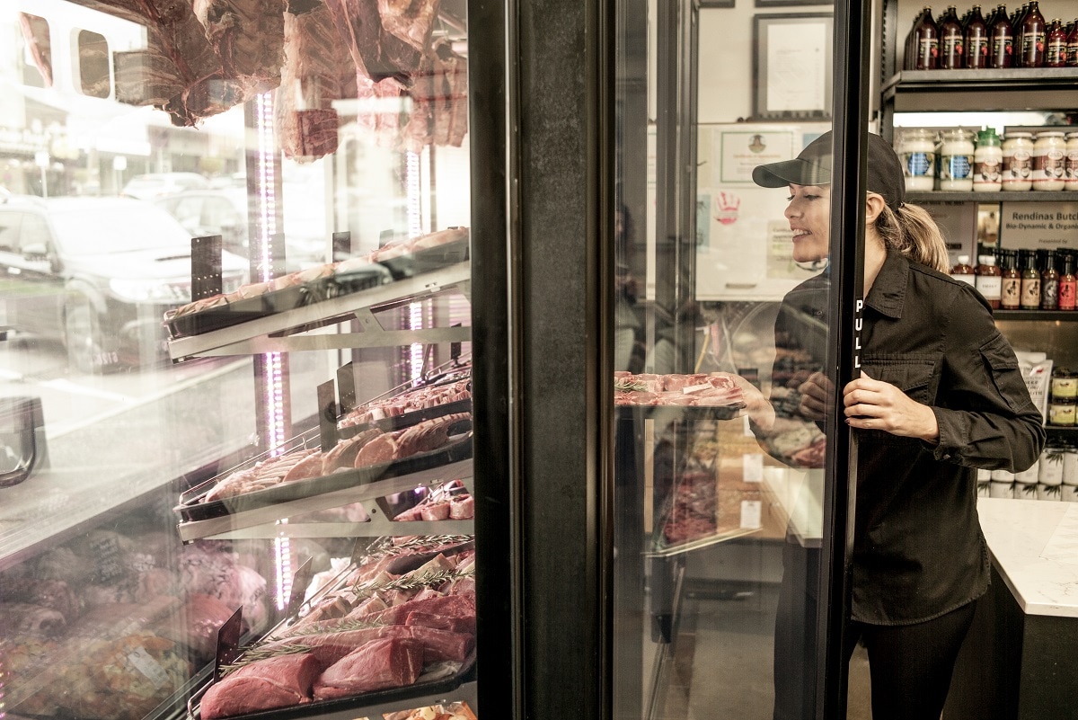 A woman works at IGA Corryong supermarket, placing stock inside a refrigerator
