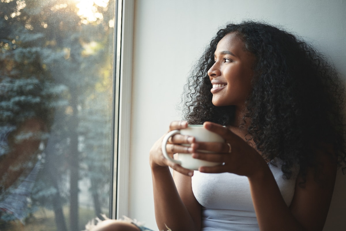 Young woman drinking tea and smiling while looking out the window