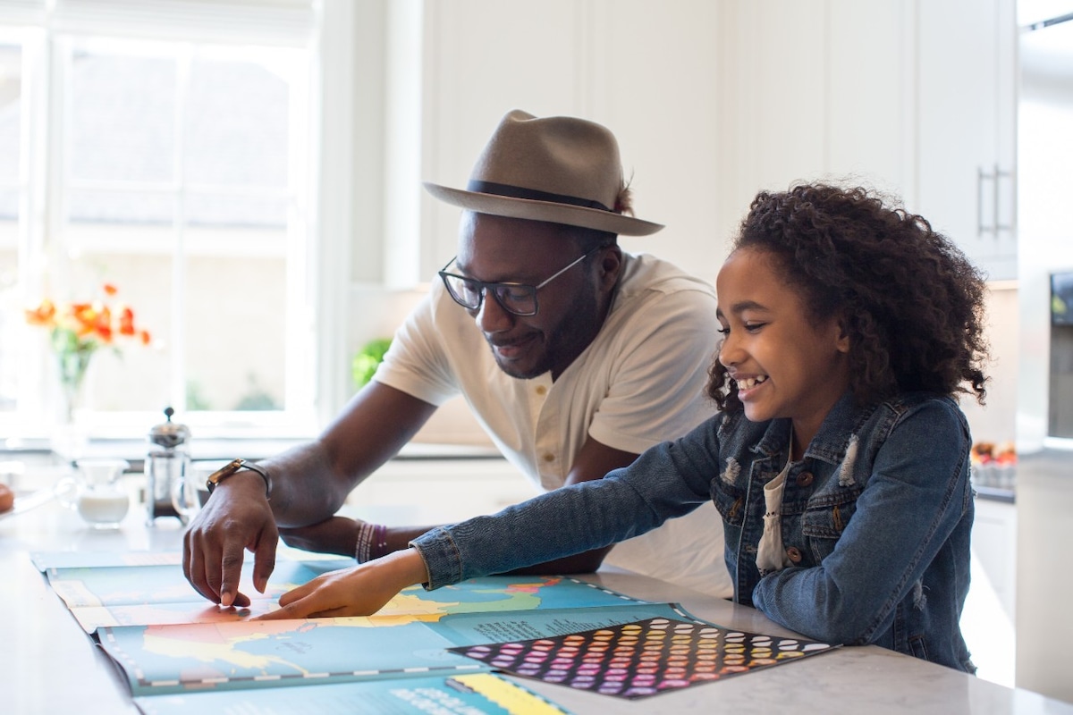 Father and daughter looking at world map on kitchen bench