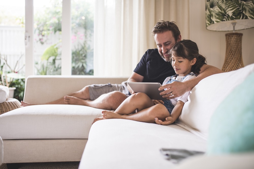 Father and daughter sitting on the couch with their tablet