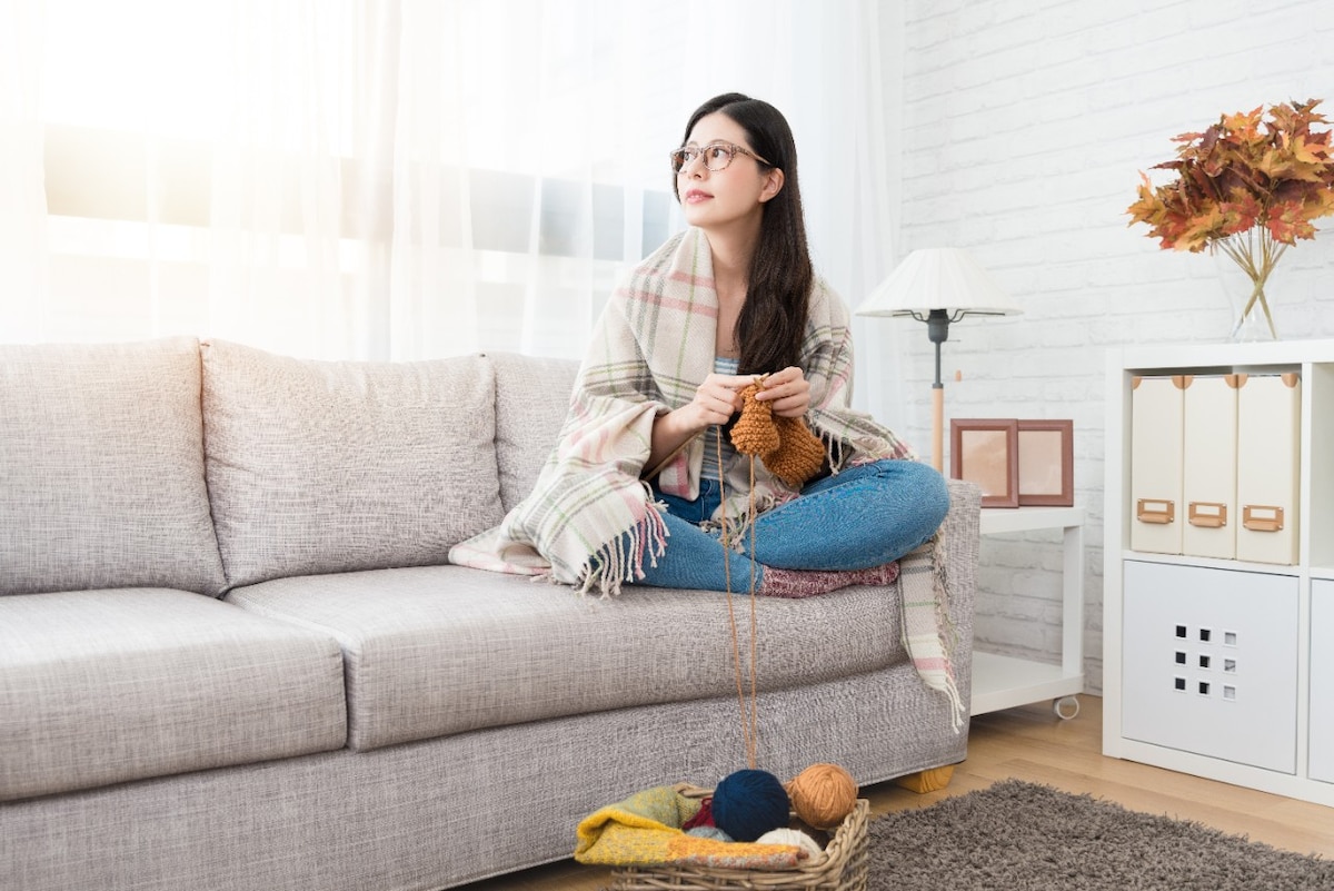 Woman rugged up and knitting on couch