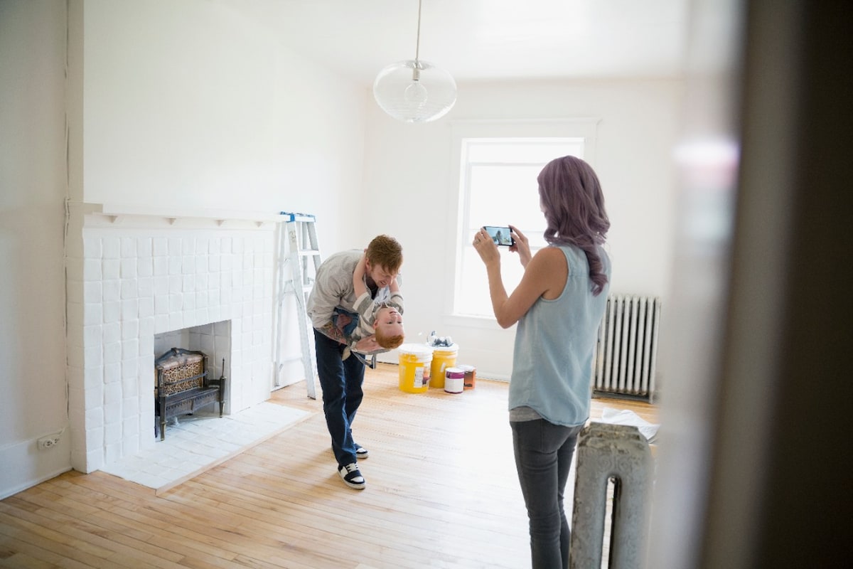 Mother photographing playful father holding son in empty new house