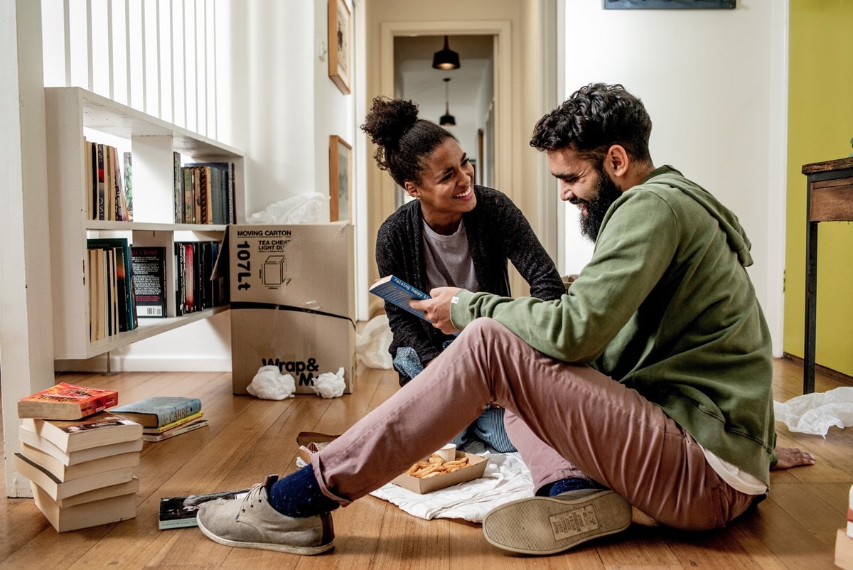 A man and a woman laughing as they unpack their collection of books into their new home