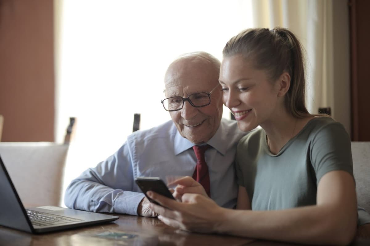 An elderly man and a young woman look at a mobile phone in her hands