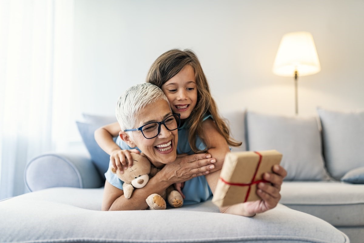 A woman and her child lay on a couch looking at a present in the woman's hands