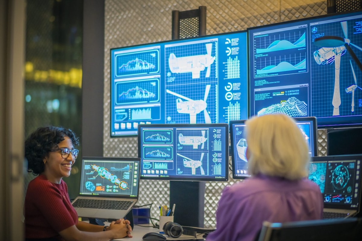 Two women discussing wind mills with the blue prints on their laptops