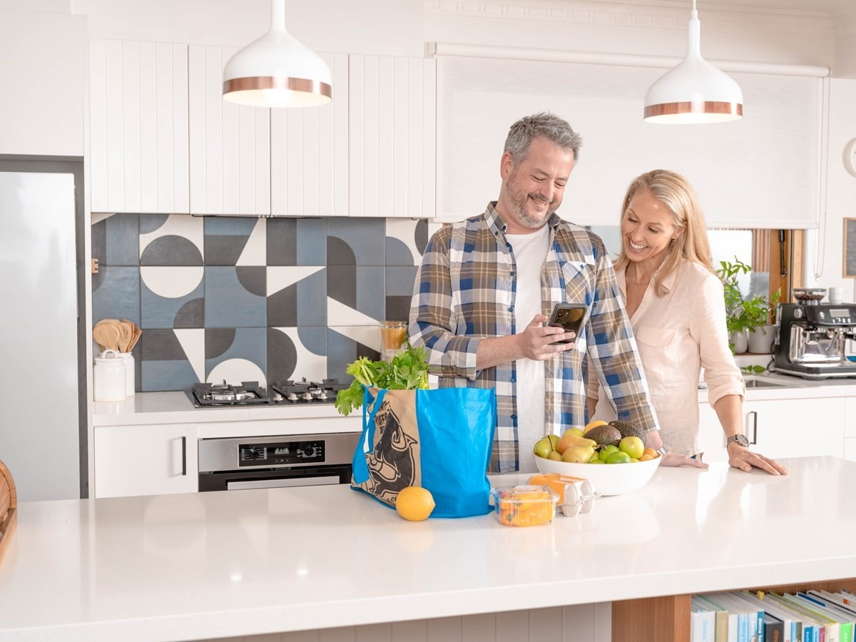 Smiling couple looking at phone with groceries on bench