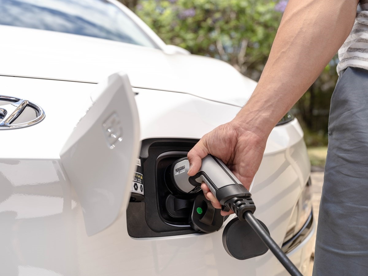 Closeup of arm holding charger into white electric car